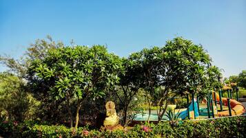Surrounded by lush greenery, a serene Buddha statue sits amidst well-manicured gardens and a family-friendly playground.