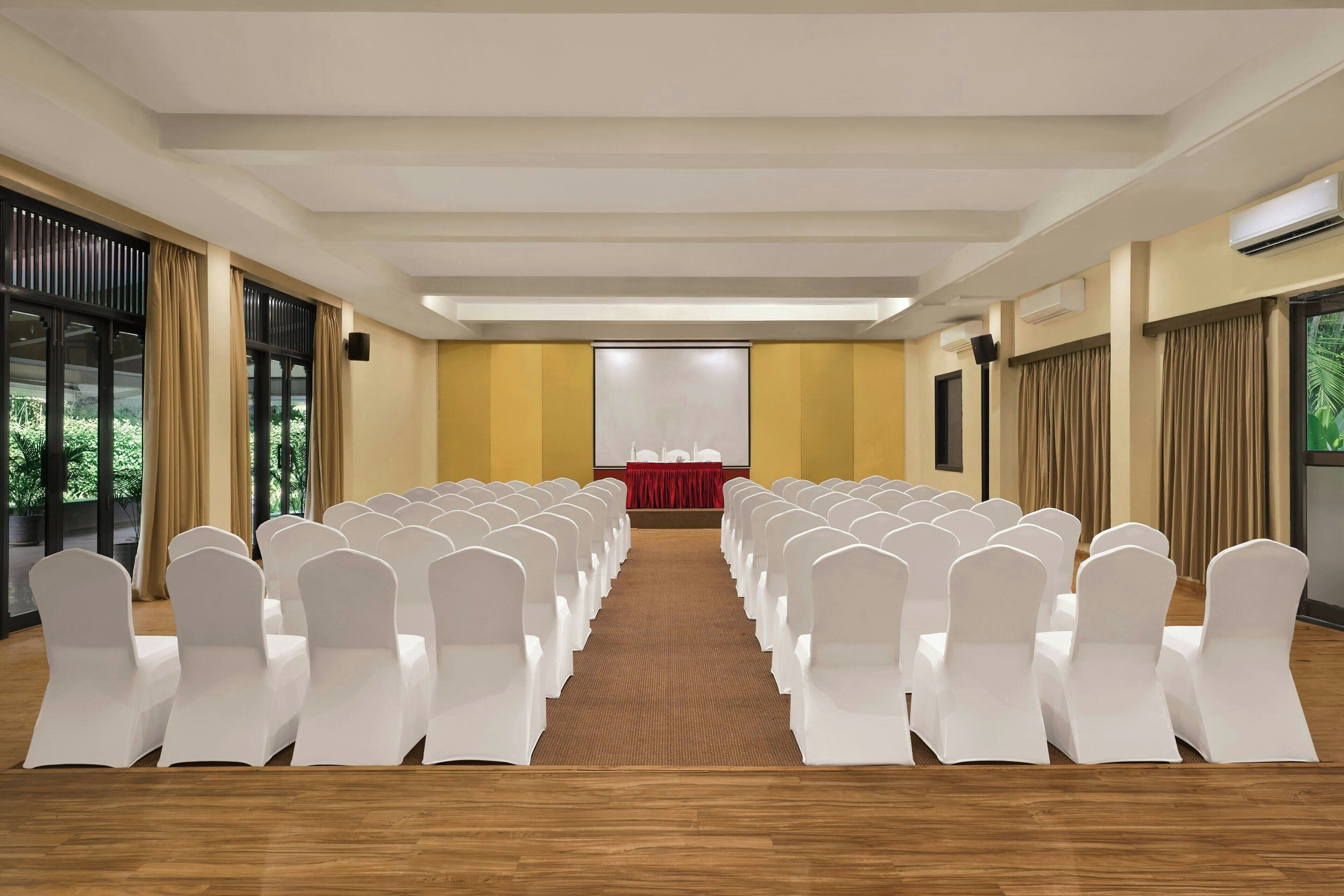 A conference room with rows of white chairs, a podium, and a red tablecloth.