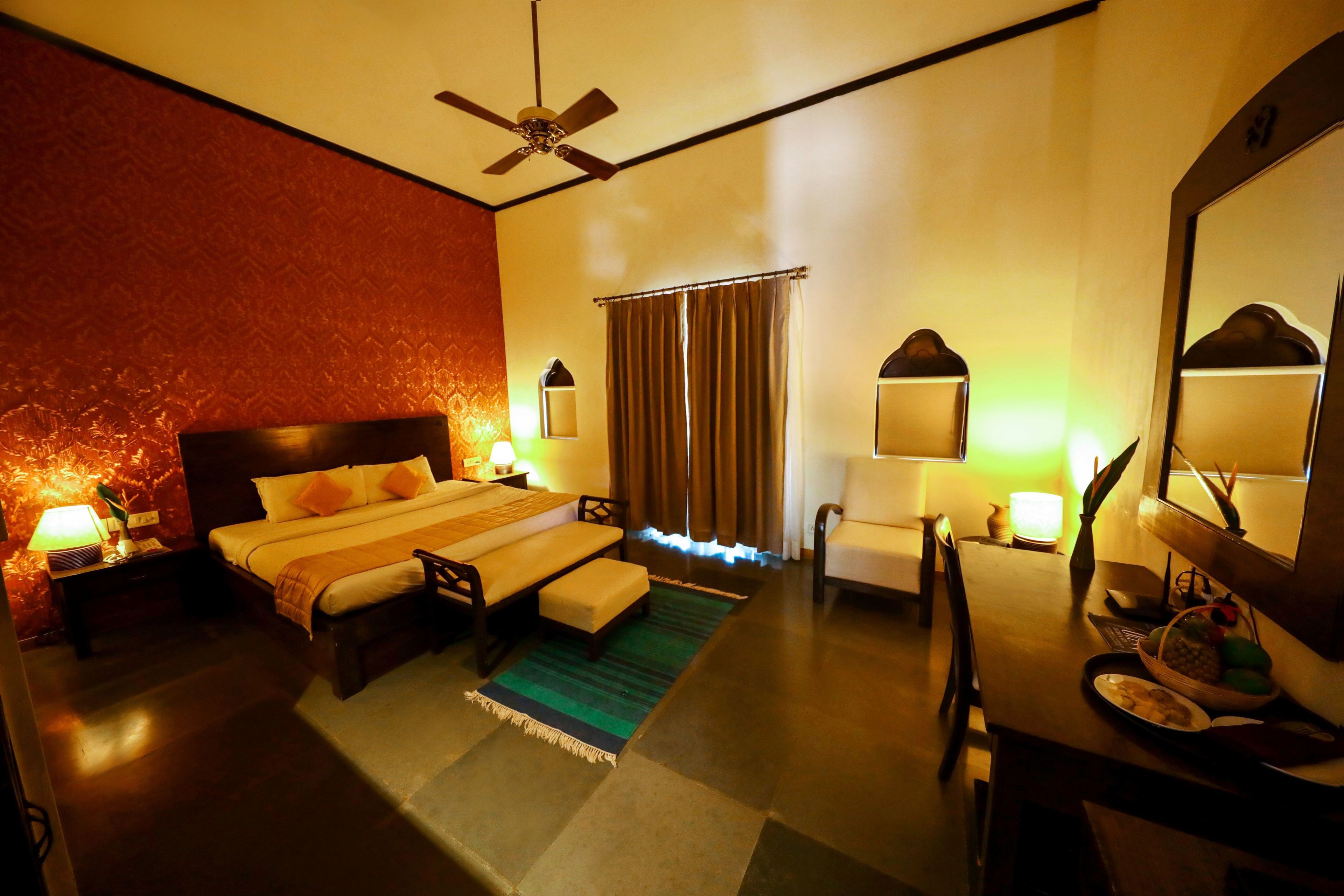 A hotel room with a bed, bedside table, lamp, chair, desk, and mirror.