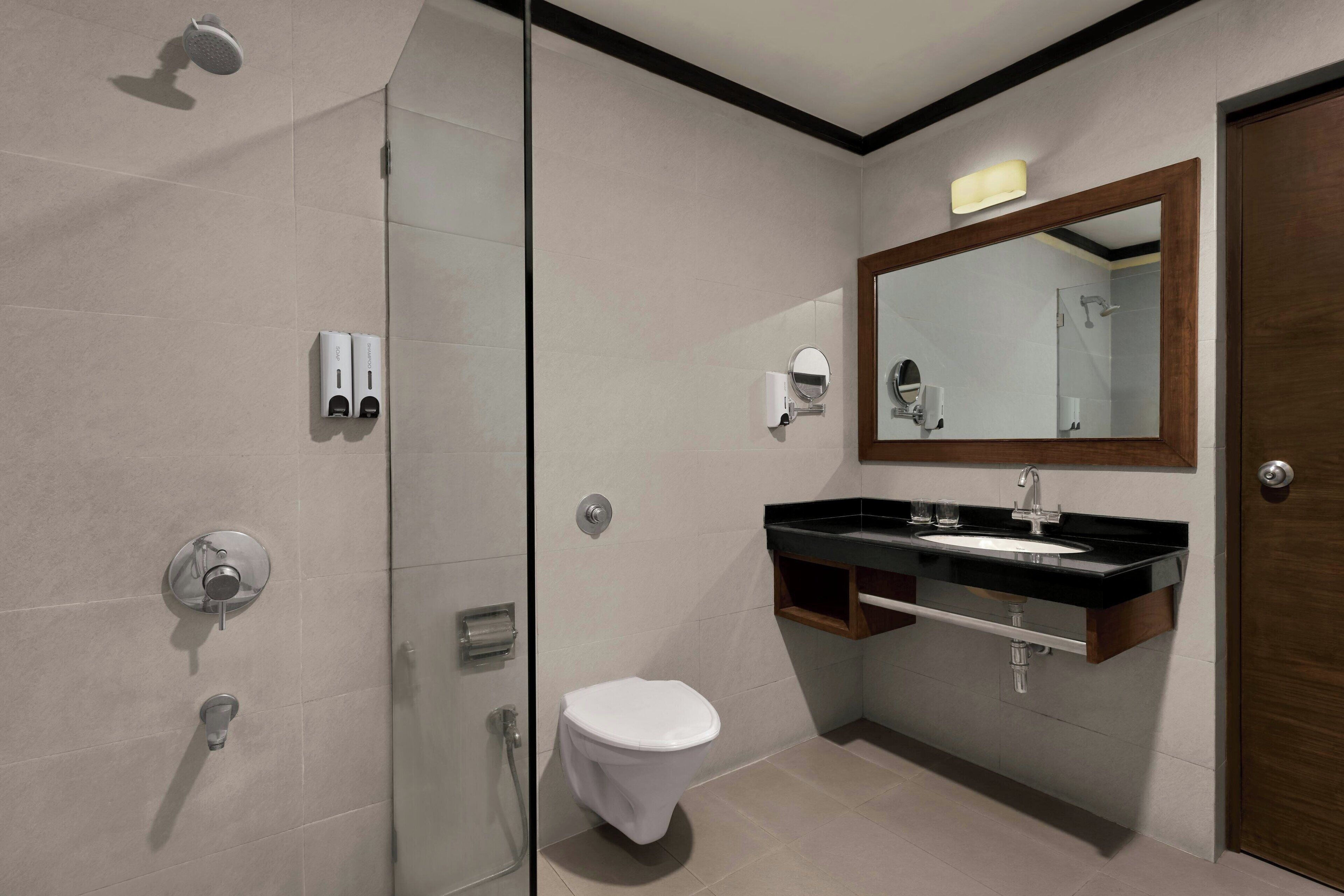 Ein modernes Badezimmer mit Duschkabine aus Glas, einer weißen Toilette, einem schwarzen Waschbecken mit Holzplatte und einem großen Spiegel über dem Waschbecken.