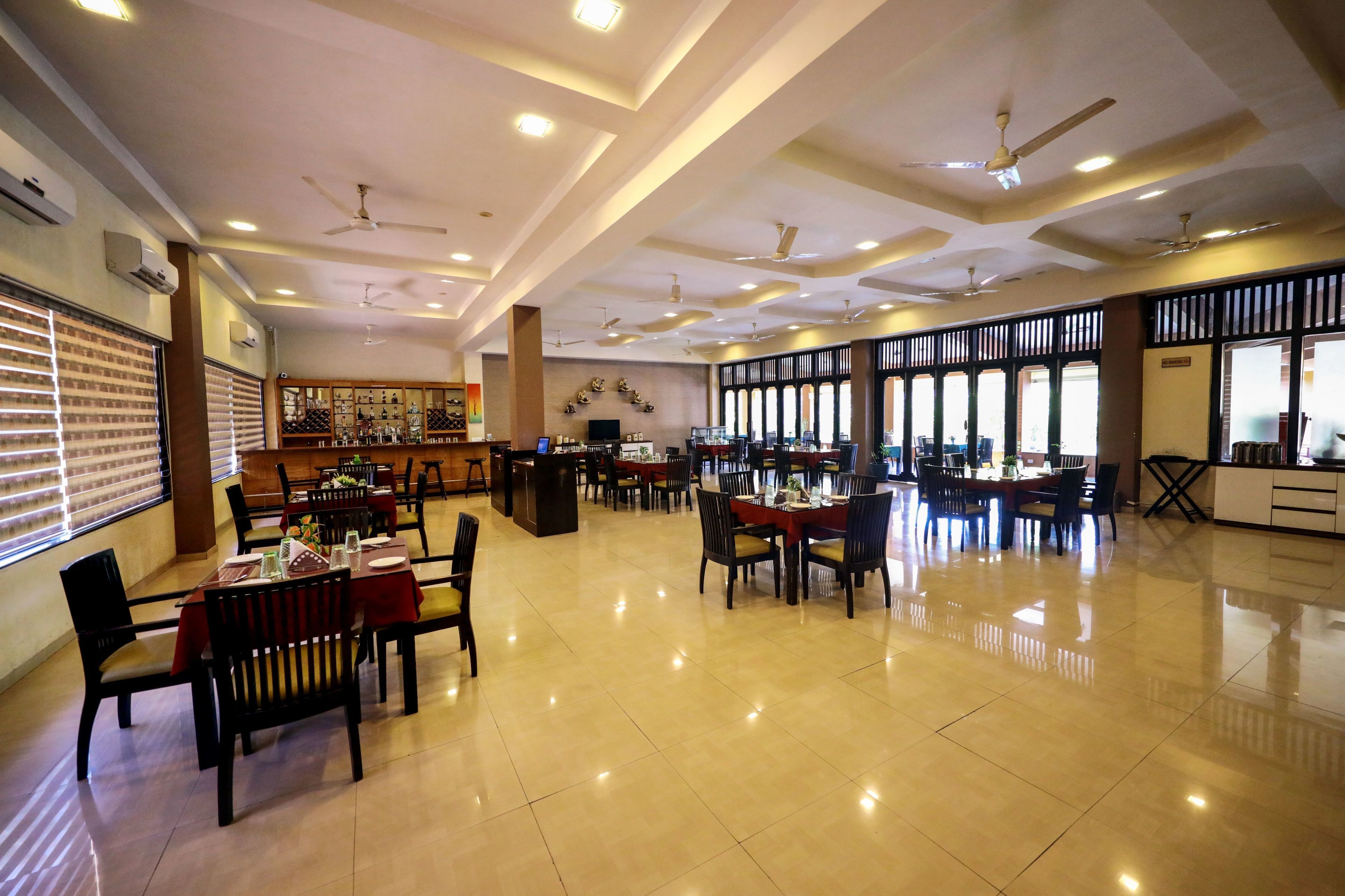 A spacious hotel dining area with multiple tables and chairs, ceiling fans, and a bar area.