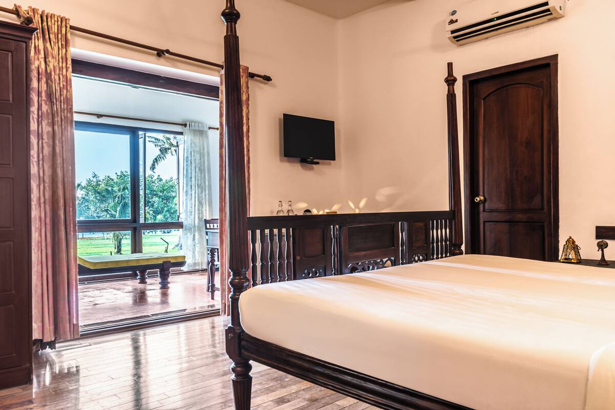 Ein Schlafzimmer mit Himmelbett, Wand-Fernseher und großem Fenster mit Vorhängen.