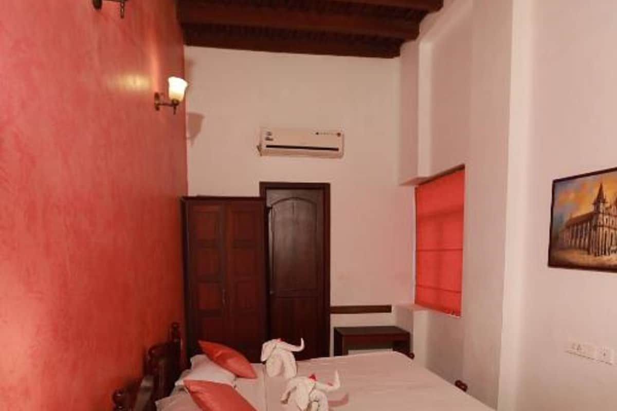 Un dormitorio con cama de madera, mesita de noche con lámpara, armario de madera y un cuadro en la pared.