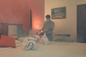 Habitación de hotel con una cama, almohadas, una mesita de noche, un cuadro en la pared y una persona de pie junto a la cama.