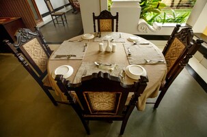 A round dining table with a beige tablecloth, surrounded by four wooden chairs with woven seats.