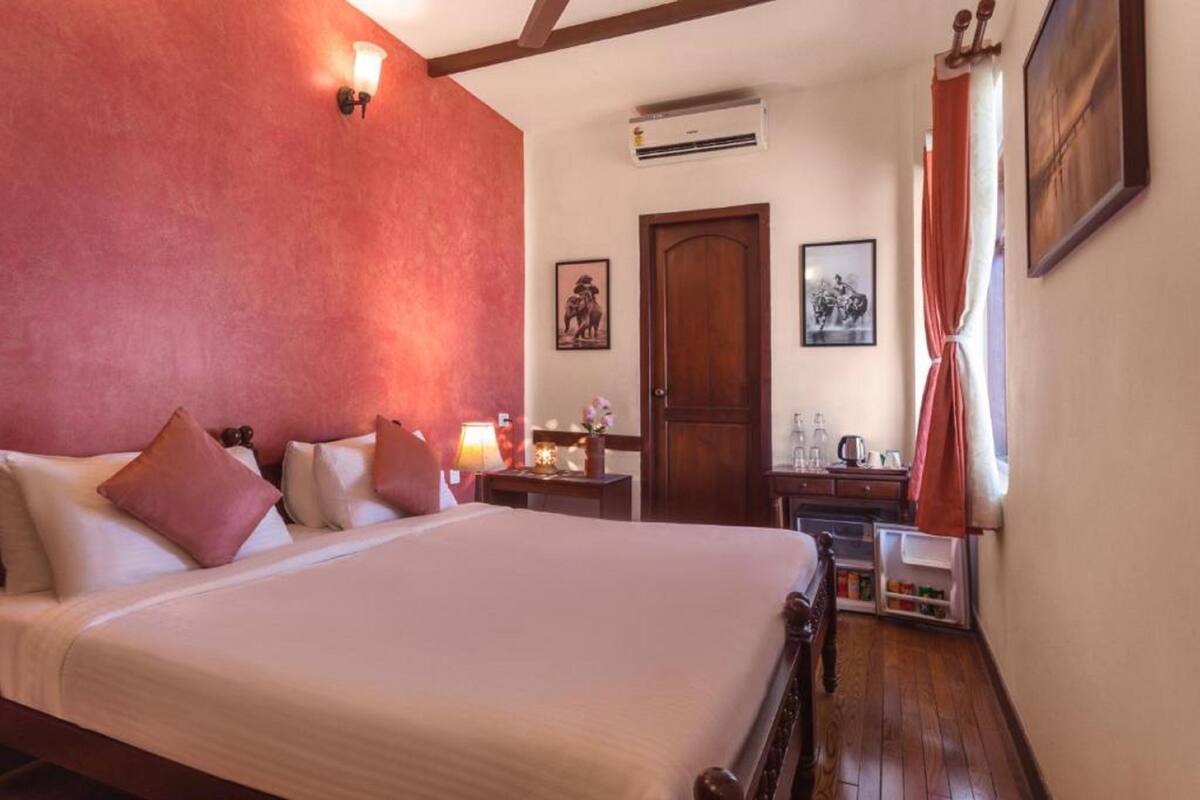 Ein Hotelzimmer mit einem großen Bett, einem hölzernen Kopfteil, einem Nachttisch mit Lampe, einem Kleiderschrank und einem kleinen Tisch mit einer Vase.