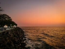 Cena costeira com uma linha de costa rochosa e mar calmo ao pôr do sol.