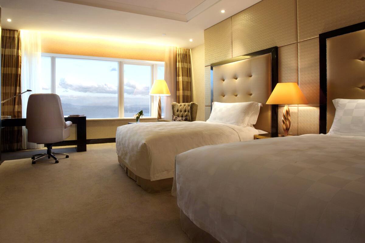 A hotel room with two beds, a desk, a chair, and a TV.