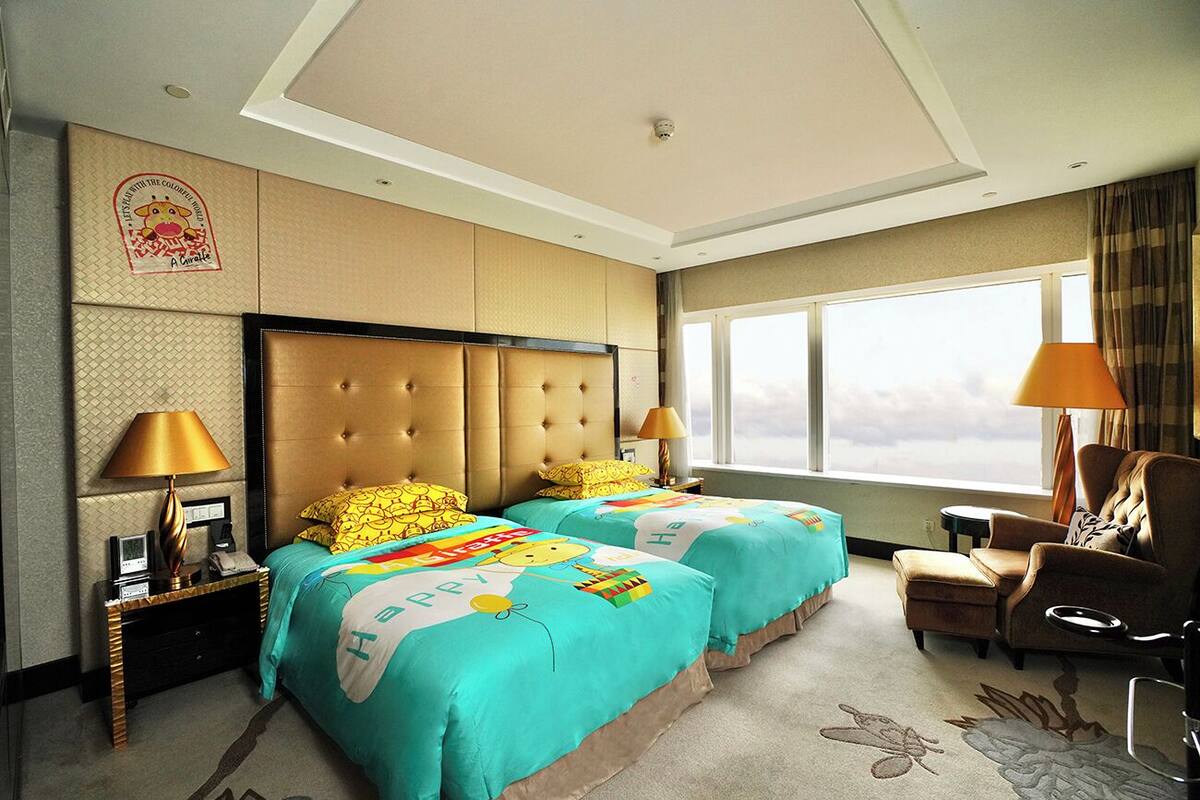 A hotel room with two beds, a sofa, a chair, a nightstand with a lamp, and a window with a view.