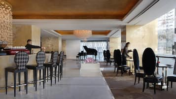 A hotel lobby with a grand piano, a bar area, and a seating arrangement with checkered chairs.