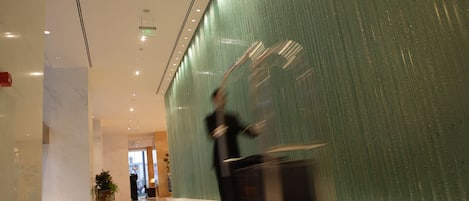 A corridor with a green textured wall, a polished floor, and a person pushing a cart.