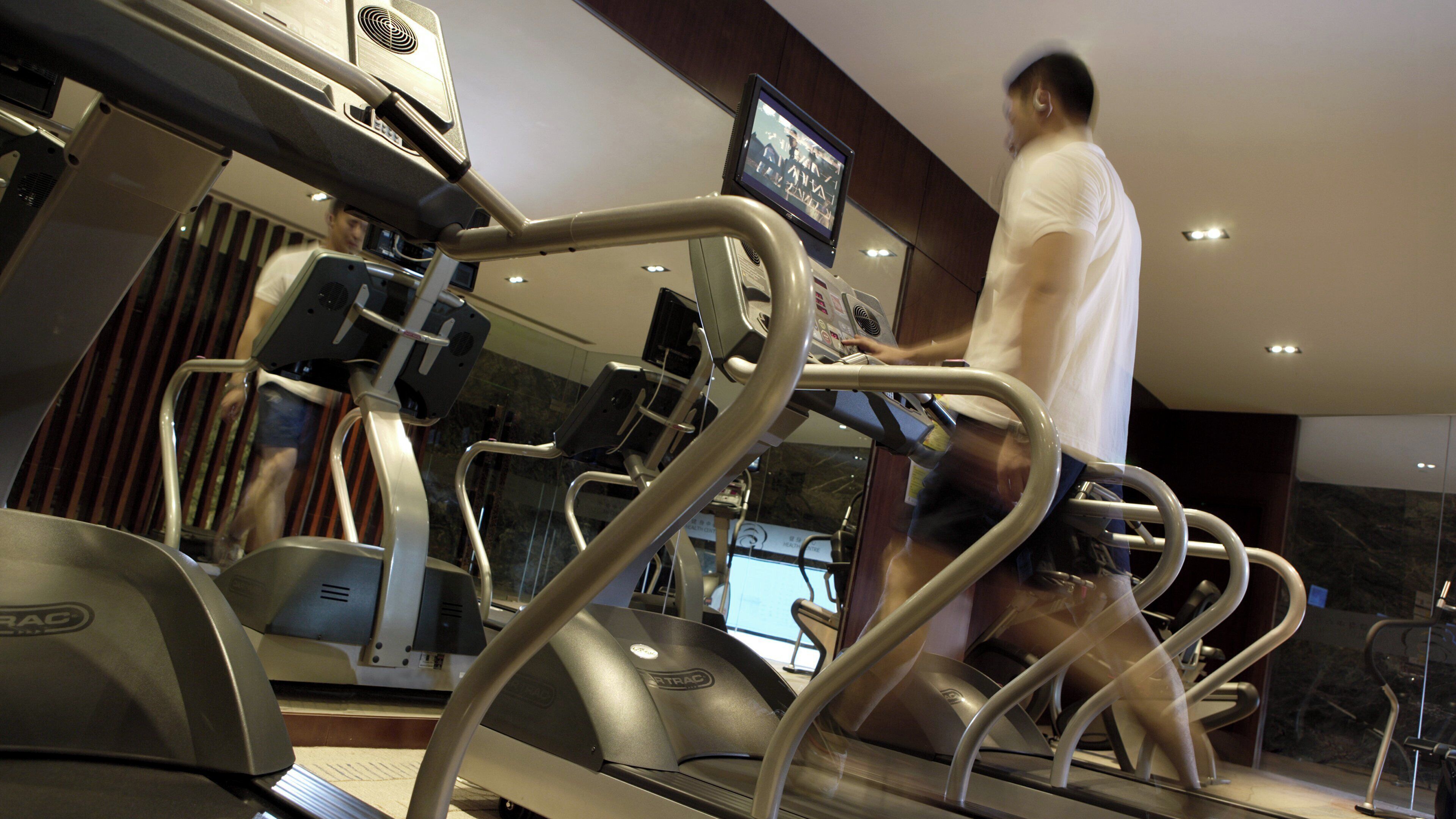 A treadmill in a gym with a digital display and a mirror.
