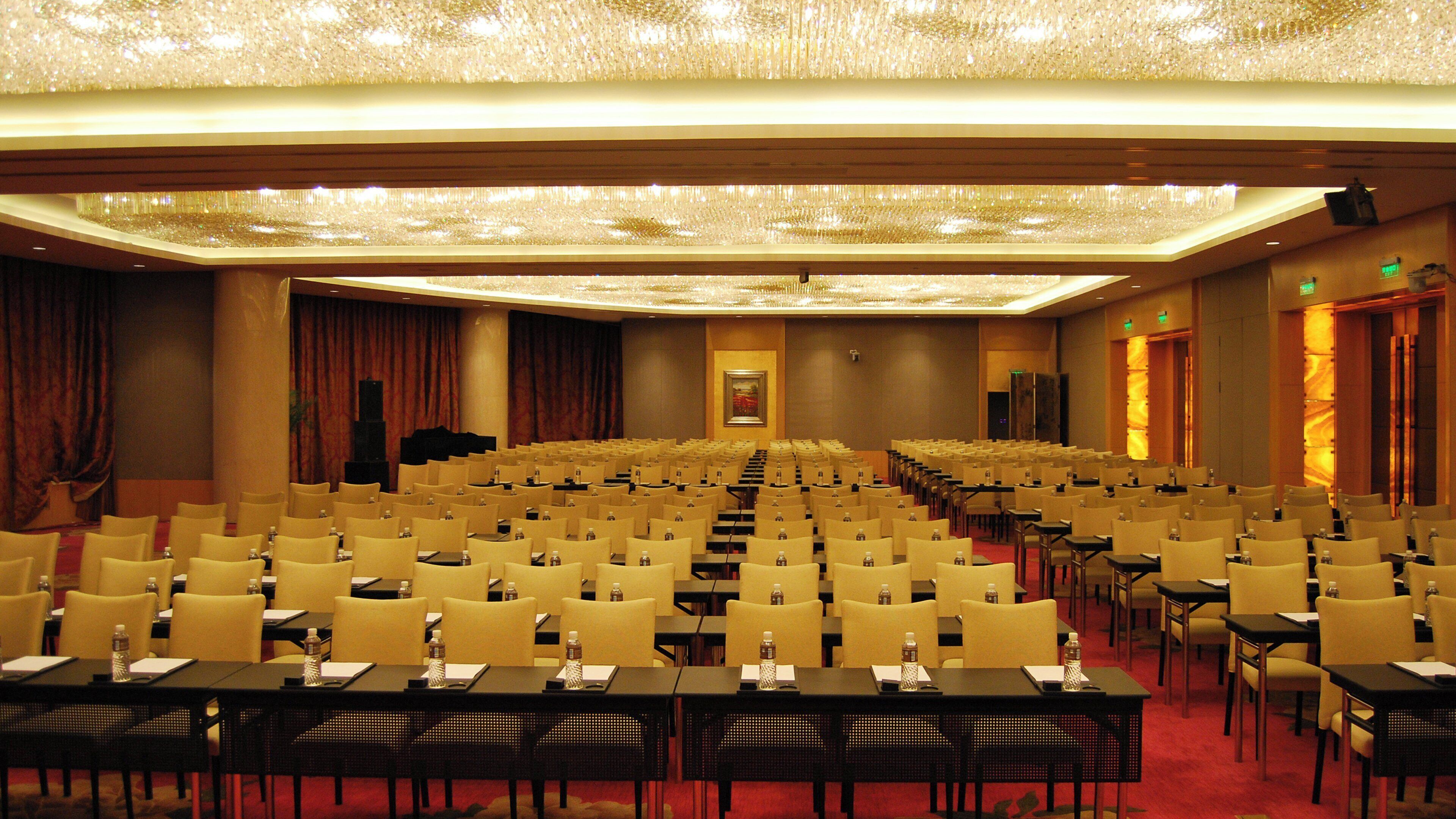 Een congreszaal met rijen stoelen en tafels, een podium en een kroonluchter.