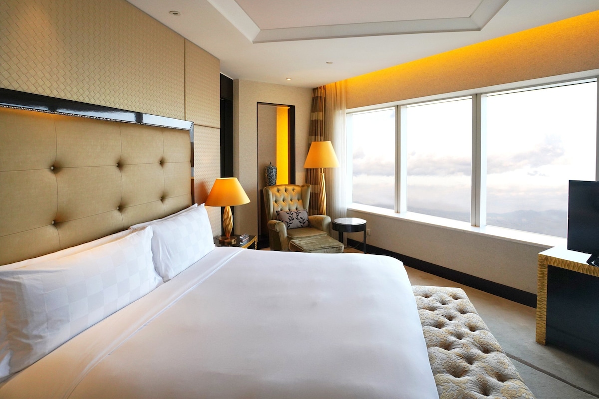 Habitación de hotel con una cama grande, televisión, silla y ventana con vistas.