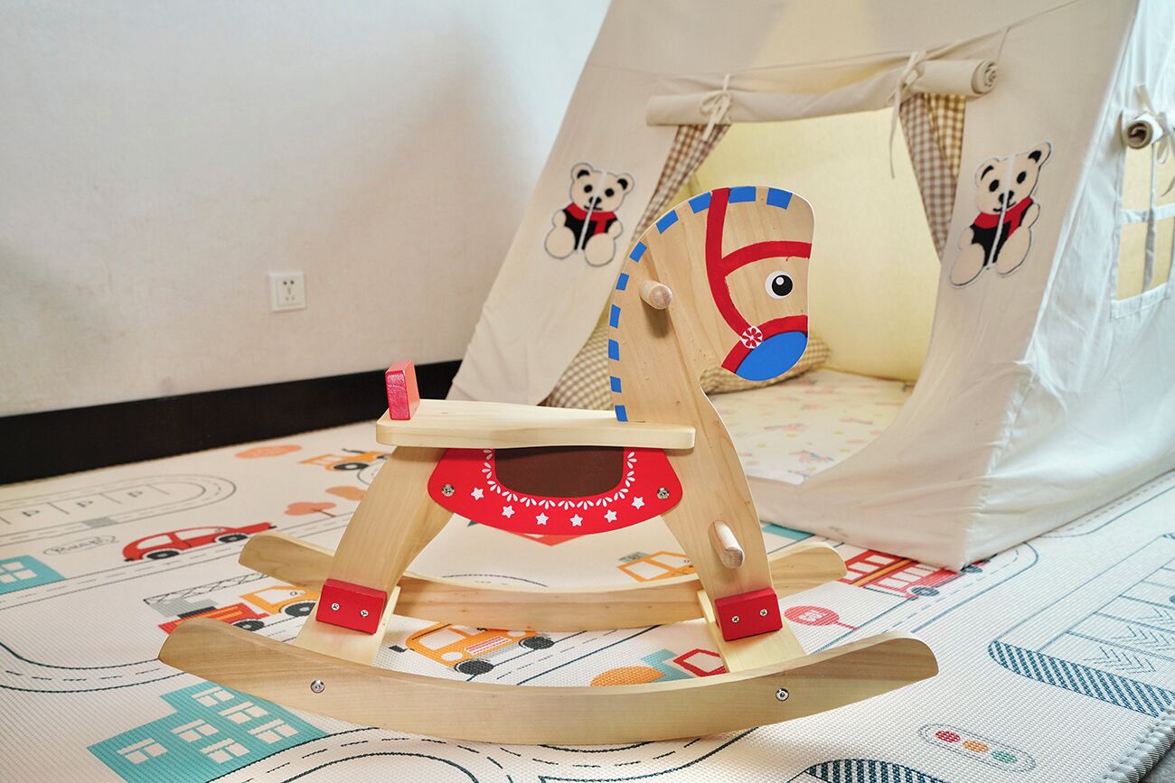 A wooden rocking chair with a red and white design, placed on a patterned rug with vehicle illustrations.