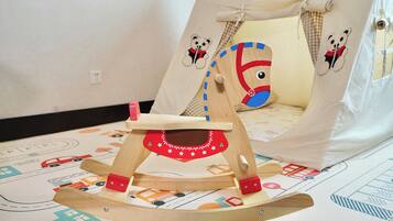 A wooden rocking chair with a red and white design, placed on a patterned rug with vehicle illustrations.