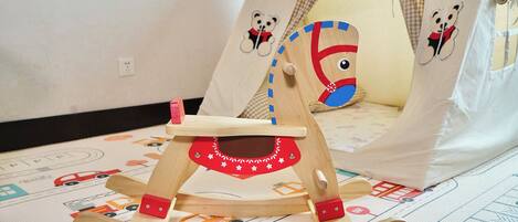 A wooden rocking chair with a red and white design, placed on a patterned rug with vehicle illustrations.