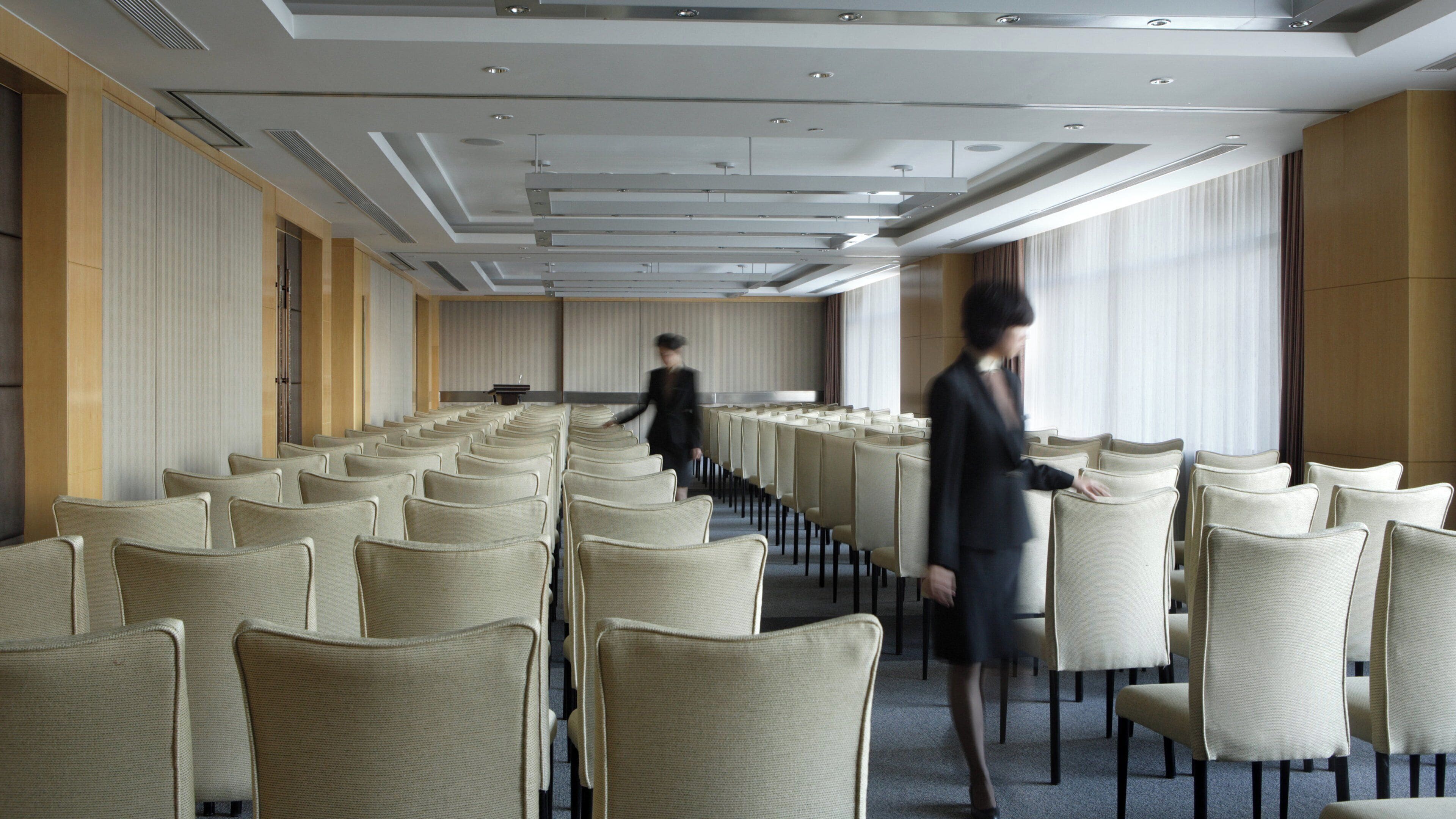 A conference room with rows of chairs, a podium, and a large window.