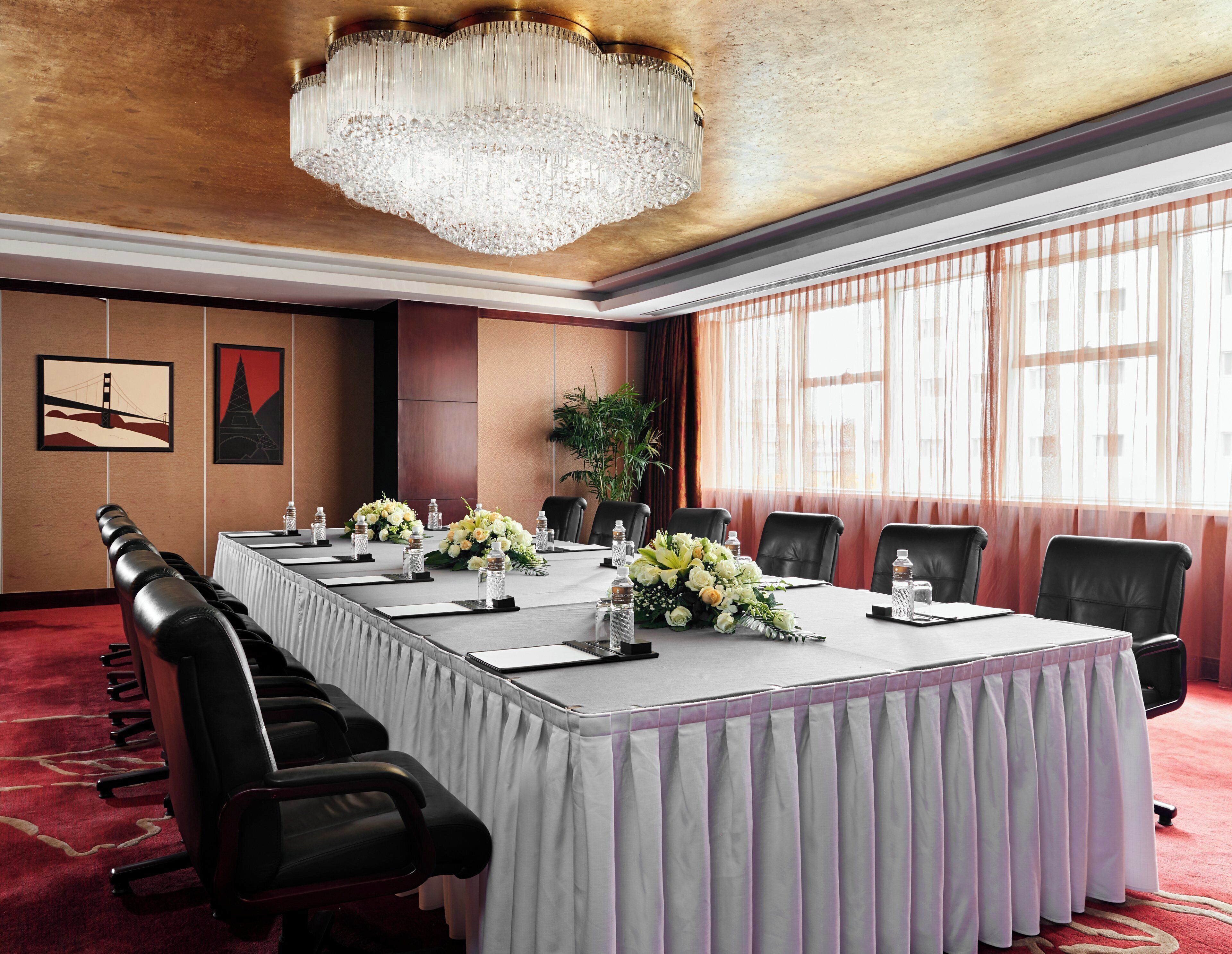 A conference room with a long table, black leather chairs, a chandelier, and artwork on the walls.