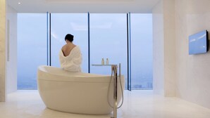 Un baño moderno con una bañera grande, una mesita con artículos de tocador y un televisor montado en la pared.