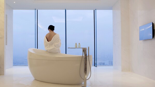 Ein modernes Badezimmer mit einer großen Badewanne, einem kleinen Tisch mit Pflegeprodukten und einem an der Wand befestigten Fernseher.