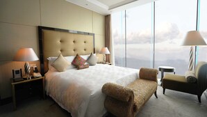 A hotel room with a large bed, two bedside tables, a chair, a small table, and a view of the city through large windows. - Intercontinental Dalian by IHG (Dalian)