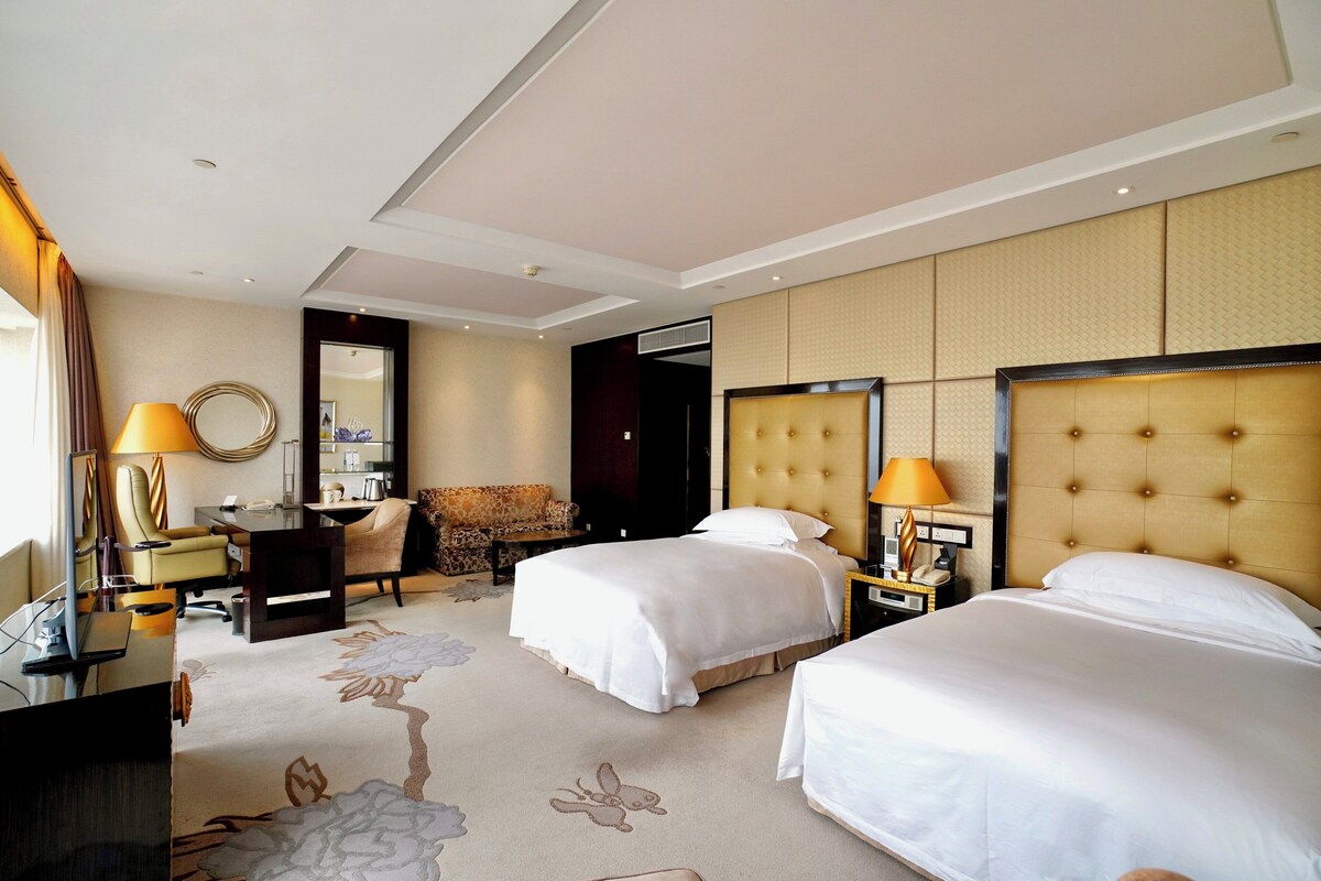Ein Hotelzimmer mit zwei Betten, einem Schreibtisch, einem Stuhl, einer Couch und einem großen Spiegel.