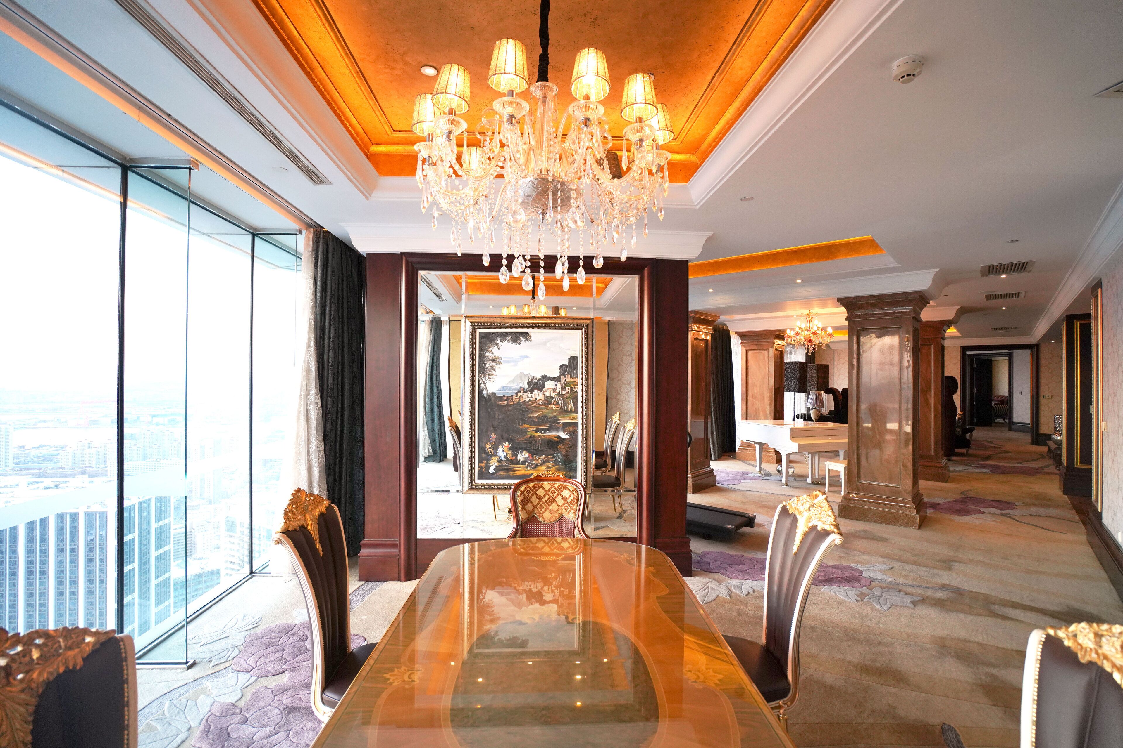 A spacious dining area with a large glass table, elegant chairs, and a chandelier.