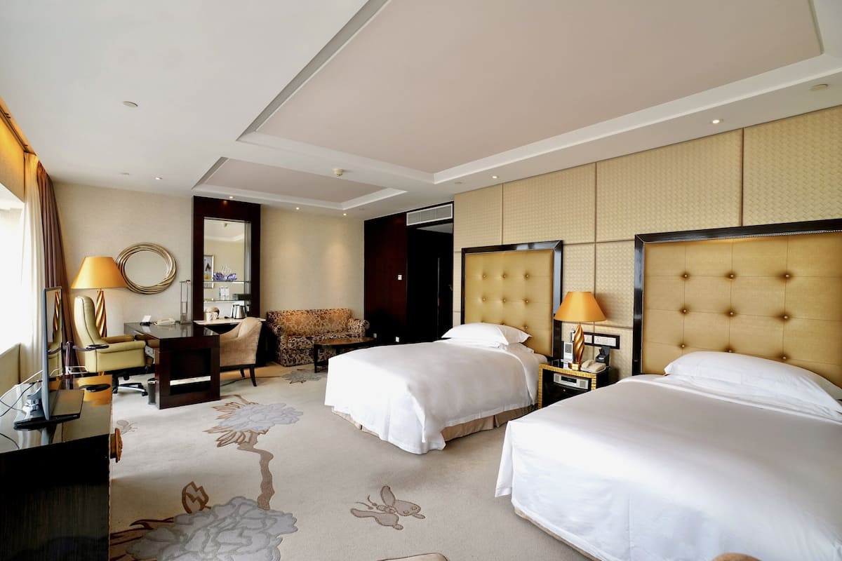 A hotel room with two beds, a desk, a chair, a sofa, and a large mirror.