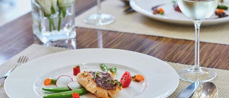 A dining table with a plate of food, a glass of white wine, and a vase of white flowers.