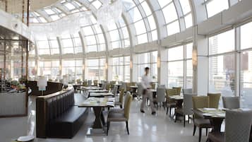 A spacious indoor area with a high ceiling and large windows, featuring seating arrangements and a reception desk.