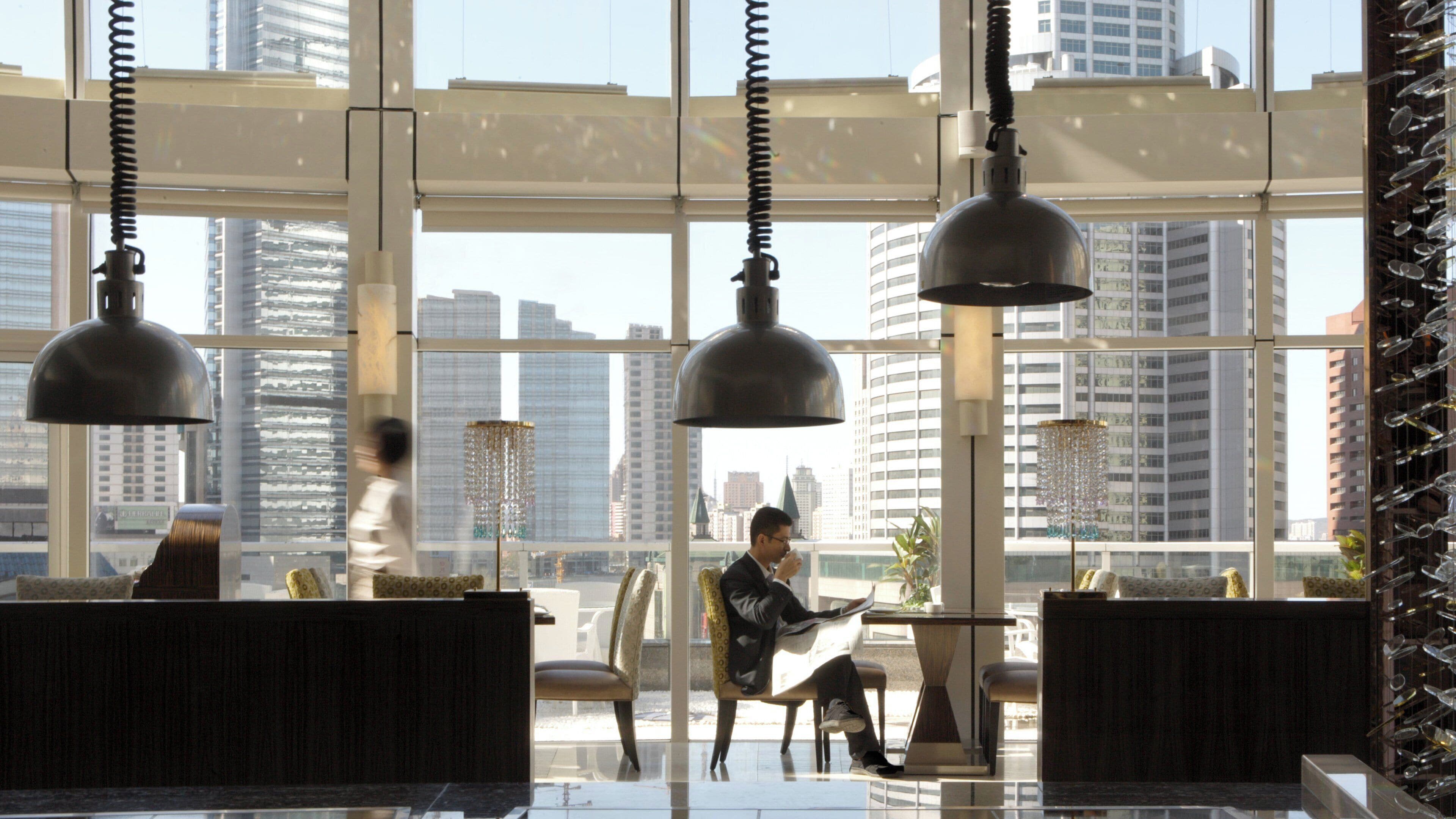 Un intérieur moderne avec de grandes fenêtres, de nombreux espaces de détente et des luminaires suspendus.