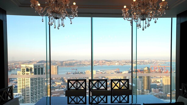 Un comedor con mesa y sillas, ventanas amplias con vista a la ciudad y candelabros.