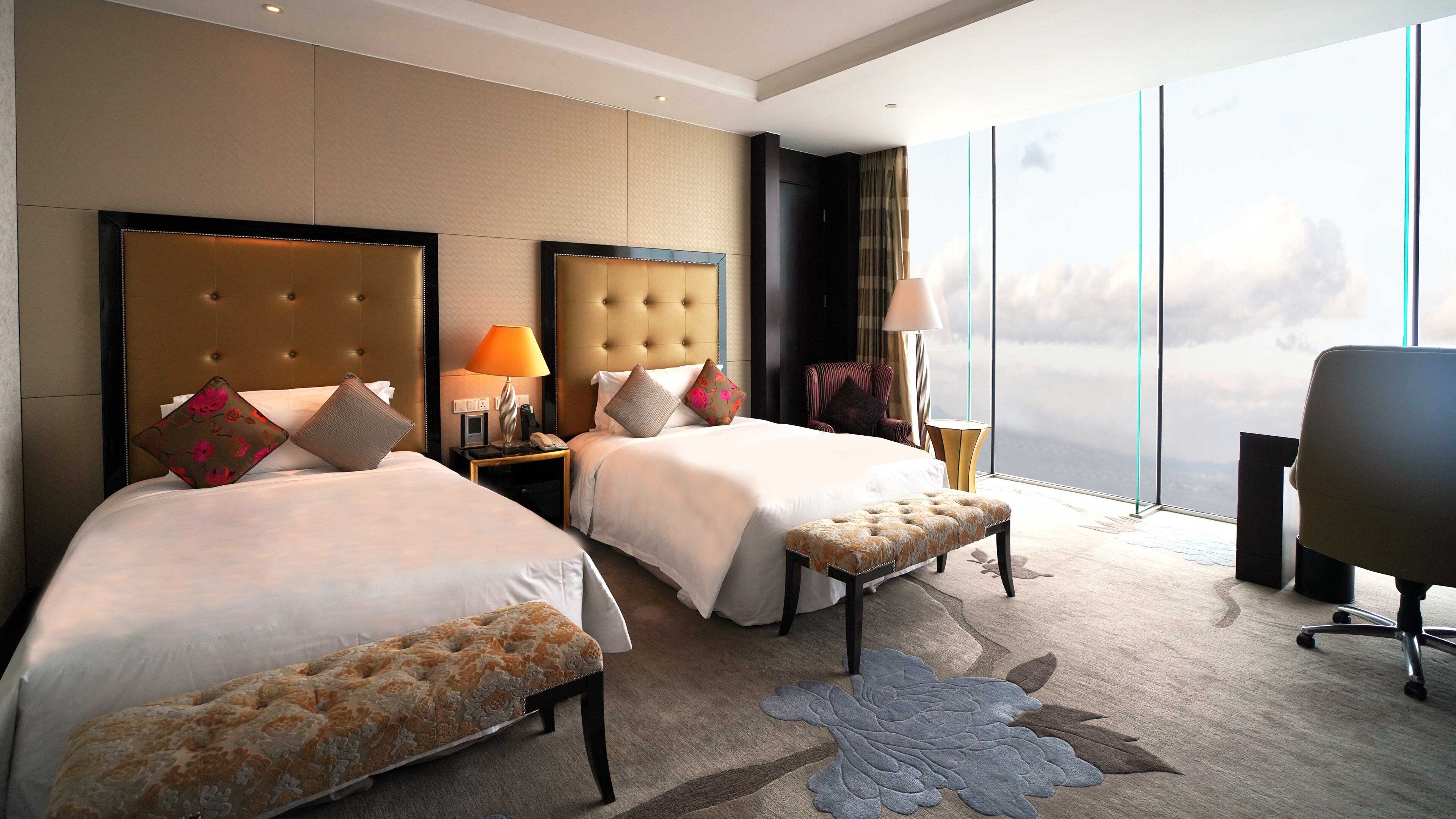 Habitación de hotel con dos camas, un ventanal grande con vista a la ciudad, un escritorio y una silla.