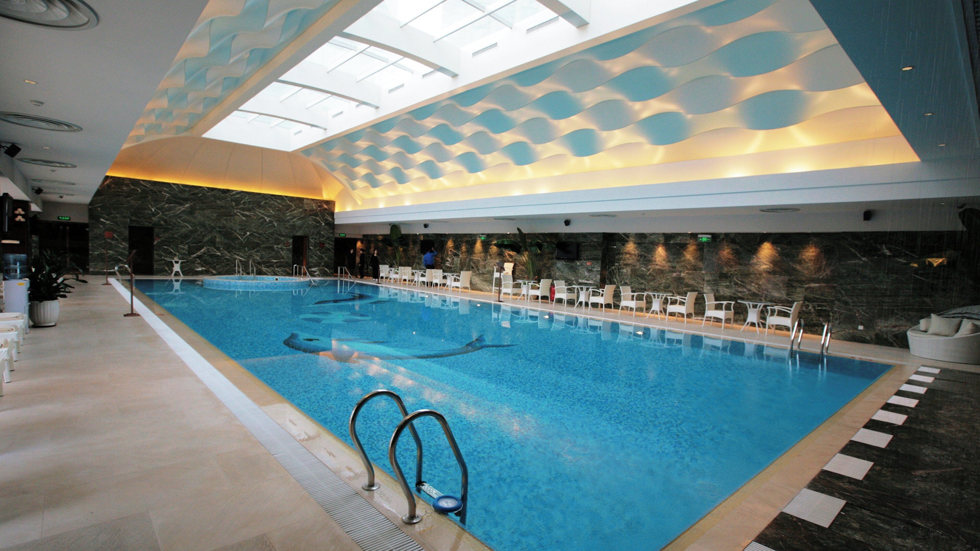 Una piscina cubierta con varias pistas de natación, una zona de estar con sillas y un techo decorativo.