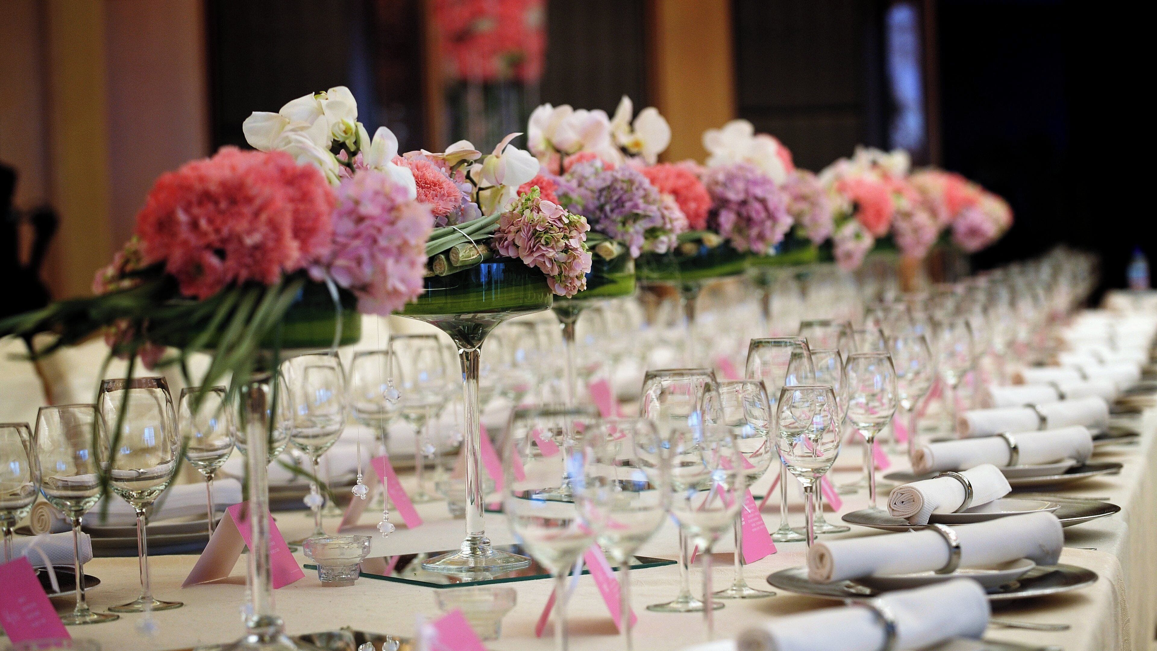 A banquet table set with multiple wine glasses and a variety of flowers.