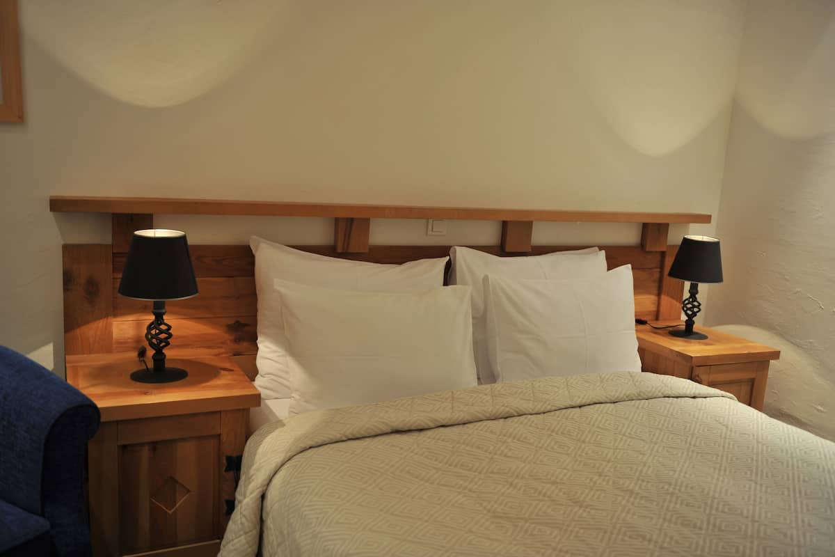 Uma cama bem arrumada com um cobertor estampado, duas mesas de cabeceira com abajures e uma cabeceira de madeira.