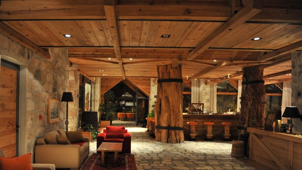 A spacious lobby with a stone floor, wooden ceiling beams, and a large wooden column. There is a bar area with stools and a counter. - Bianca Resort & Spa (Kolašin)