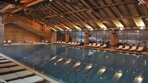 An indoor swimming pool with wooden beams, lounge chairs, and a clear view of the pool area. - Bianca Resort & Spa (Kolašin)