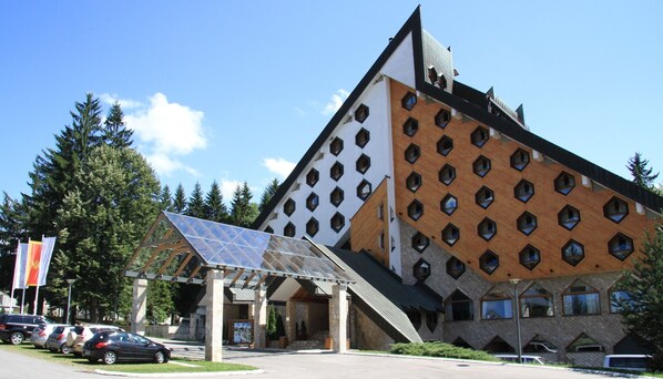 A modern building with a unique geometric facade, solar panels, and a parking area.