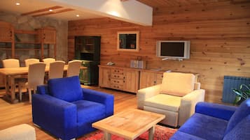 Un salon chaleureux avec des canapés bleus et beiges, une table basse en bois, un téléviseur et un mur en pierre.