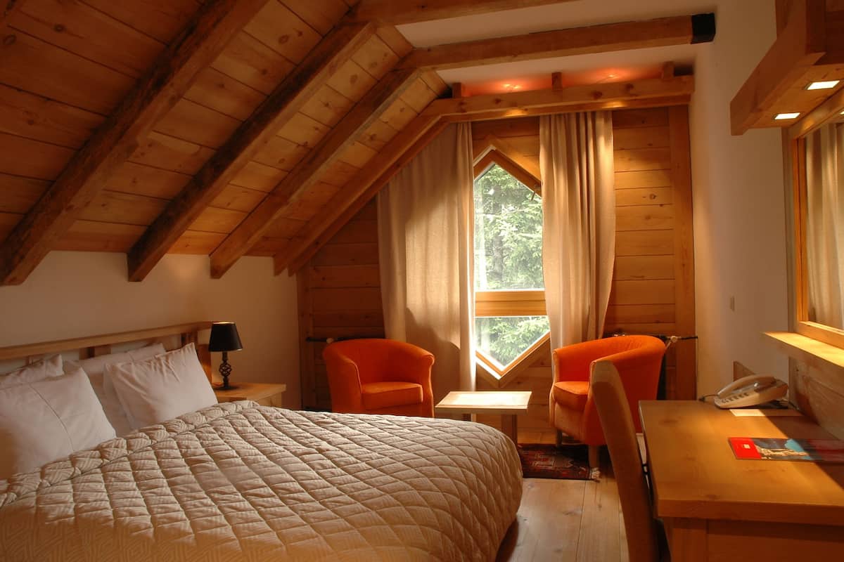 Um quarto acolhedor com cama, duas cadeiras, uma mesa pequena e uma janela com cortinas.