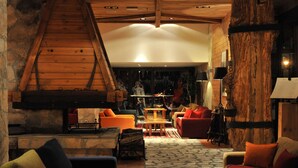 A cozy living room with a stone fireplace, wooden beams, and a variety of seating options including a sofa and chairs. - Bianca Resort & Spa (Kolašin)