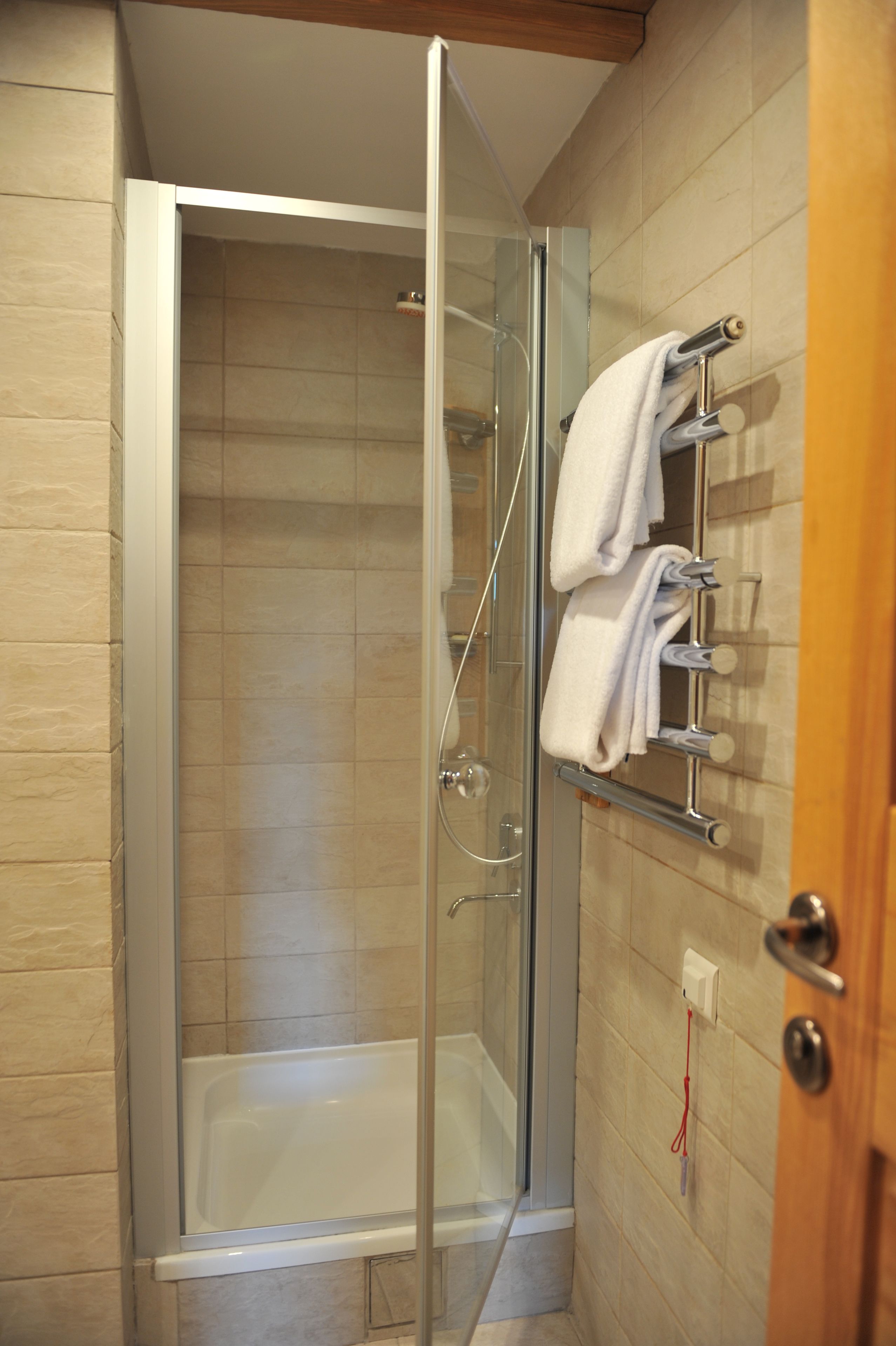 A glass-enclosed shower with a built-in bathtub, a towel rack with towels, and a wooden door.