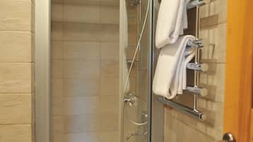 A glass-enclosed shower with a built-in bathtub, a towel rack with towels, and a wooden door.