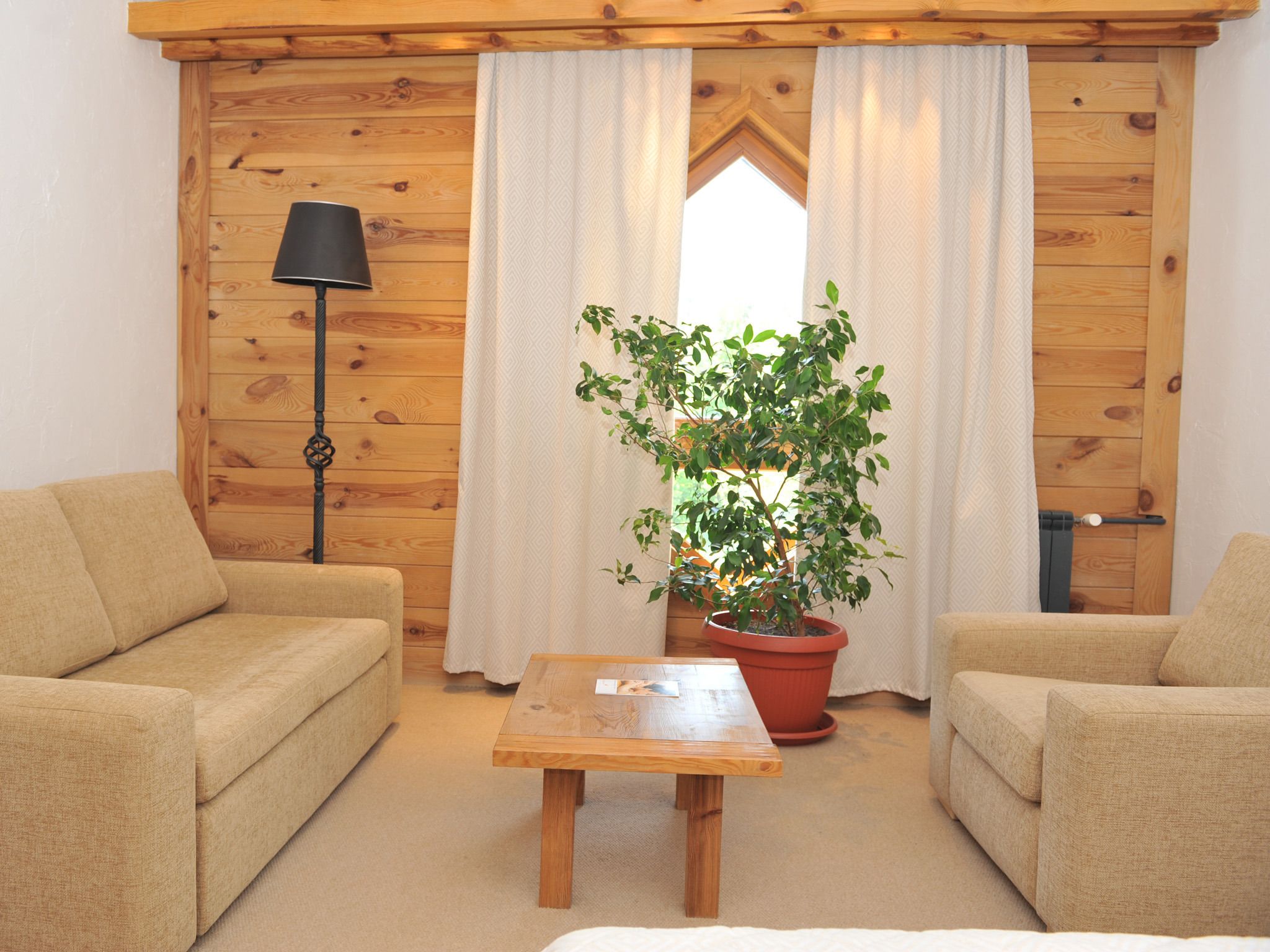 Une pièce chaleureuse avec des murs en bois, deux canapés beige, une table basse en bois, une plante en pot et un lampadaire.
