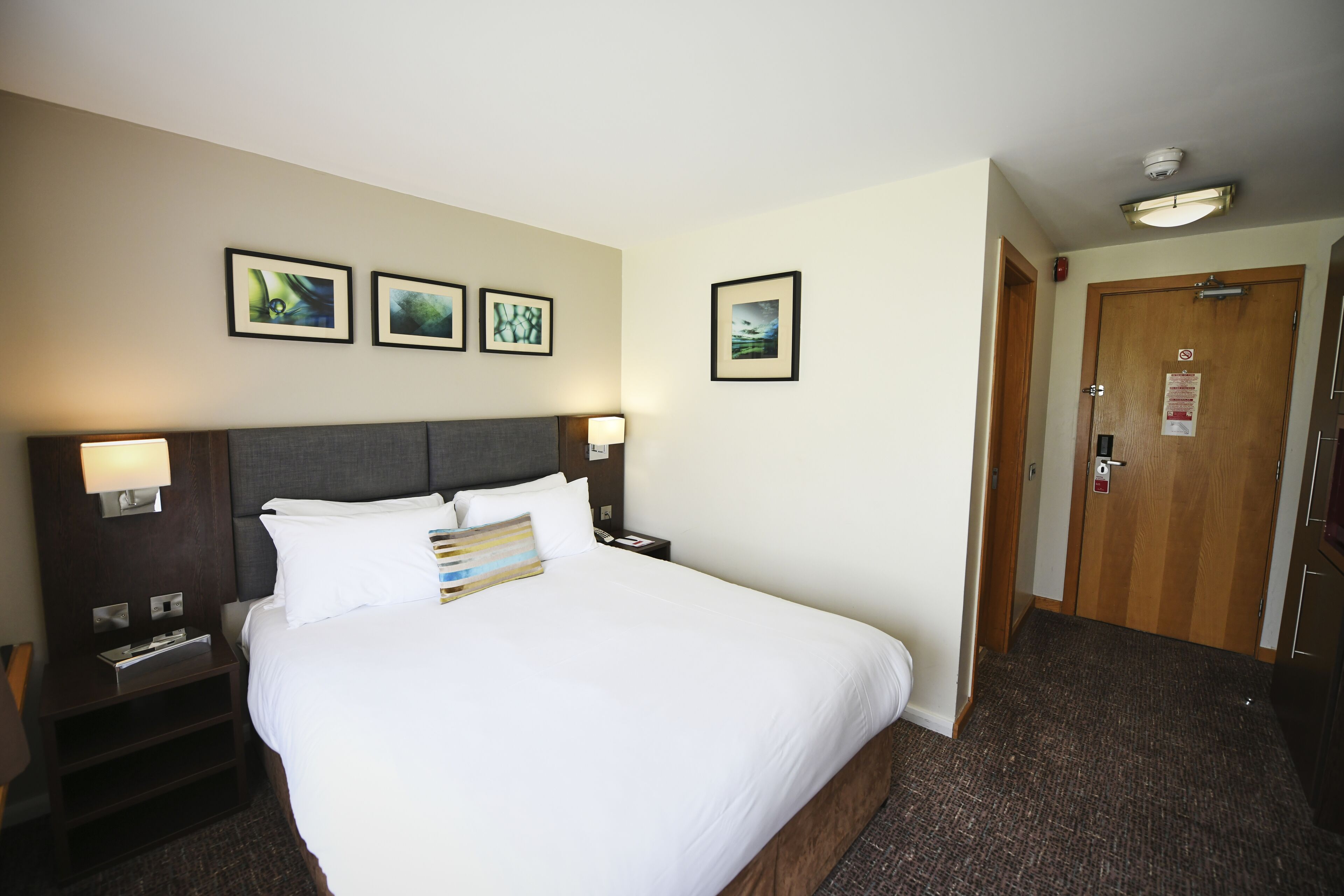 A hotel room with a large bed, bedside tables, a nightstand, and a door with a sign.