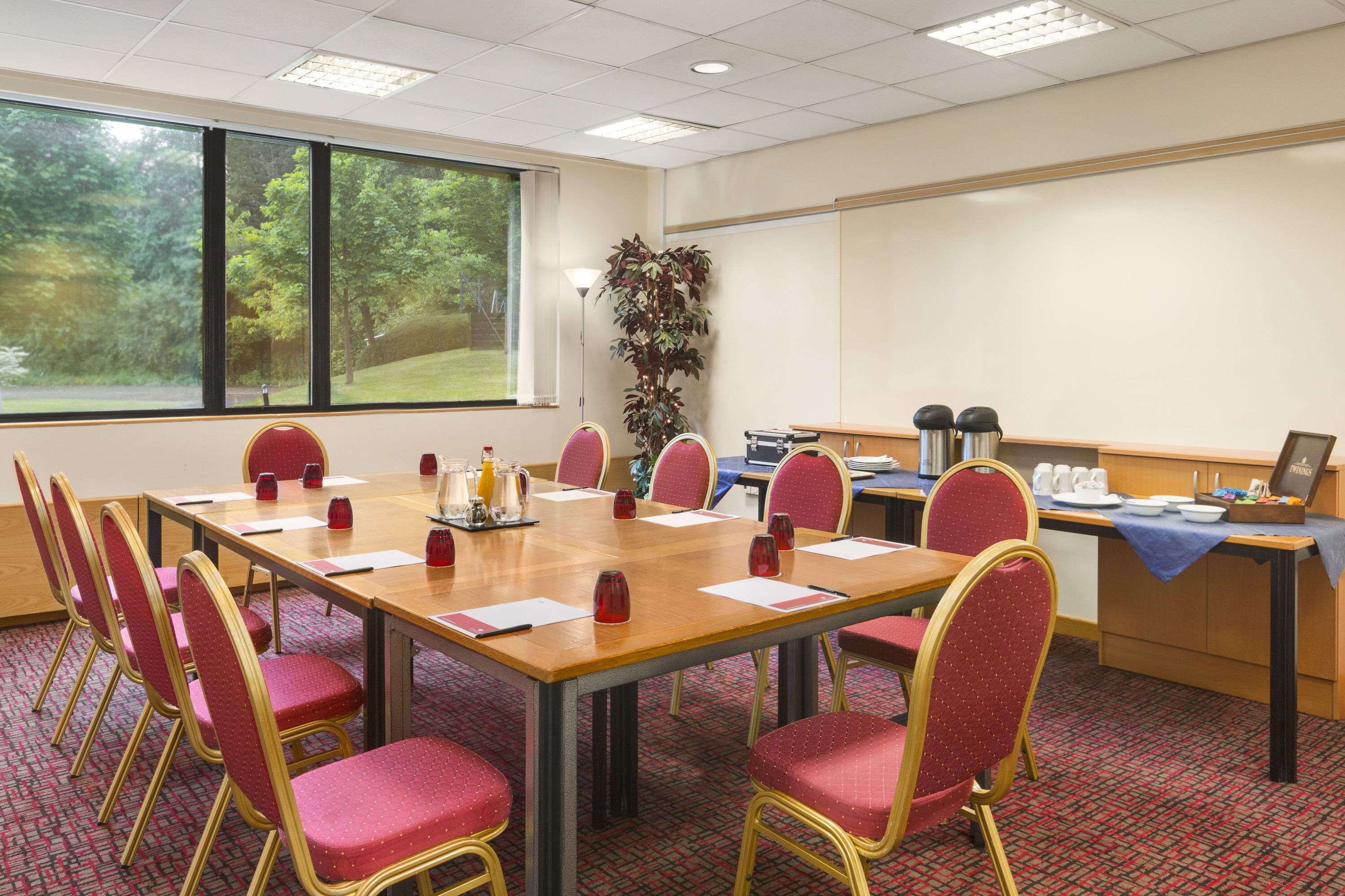 Un salón de conferencias con una mesa larga, sillas rojas, una planta y una kitchenette.