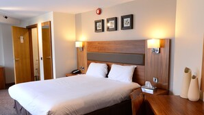 Quarto de hotel com uma cama grande, cabeceira de madeira, abajures e mesa de cabeceira com luminária.