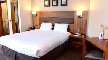 Ein Hotelzimmer mit einem großen Bett, einem Holzkopfschild, Nachttischen und einem Beistelltischchen mit Lampe.